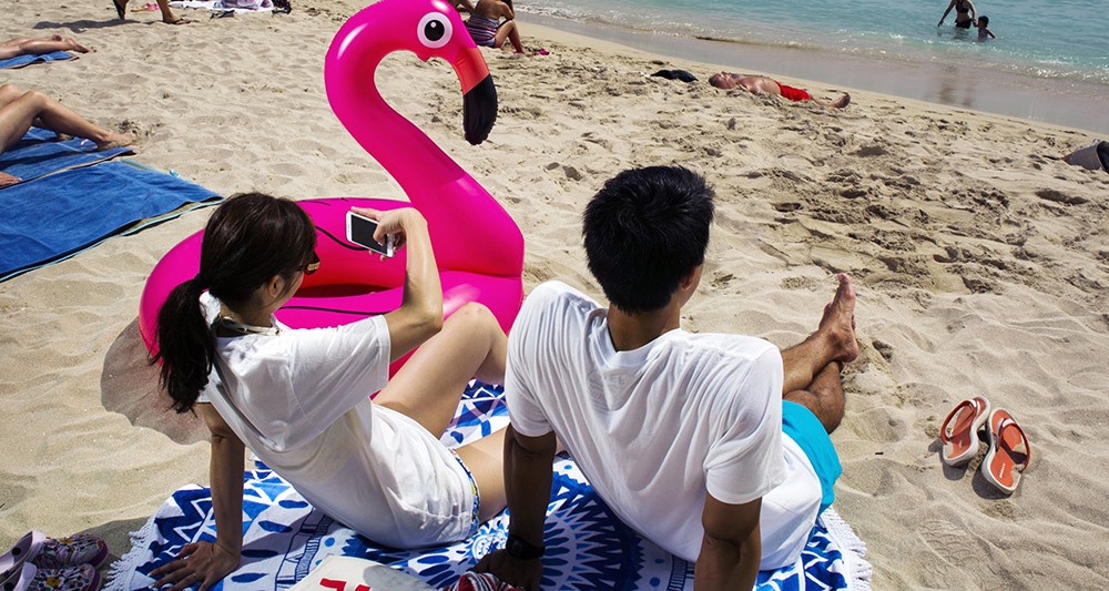 Tourists with a pink flamingo floatie on Waikiki Beach, Oahu, Hawaii. *** Local Caption *** travel Hawaii beach Waikiki Oahu vacation tourism tourist tourists floatie flamingo selfie cell phone cellphone mobile phone couple